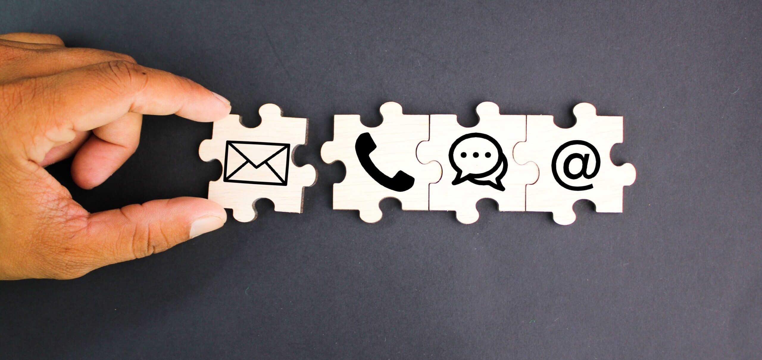 Fingers placing a puzzle piece depicting an email symbol next to pieces with a phone, chat clouds, and at symbol.