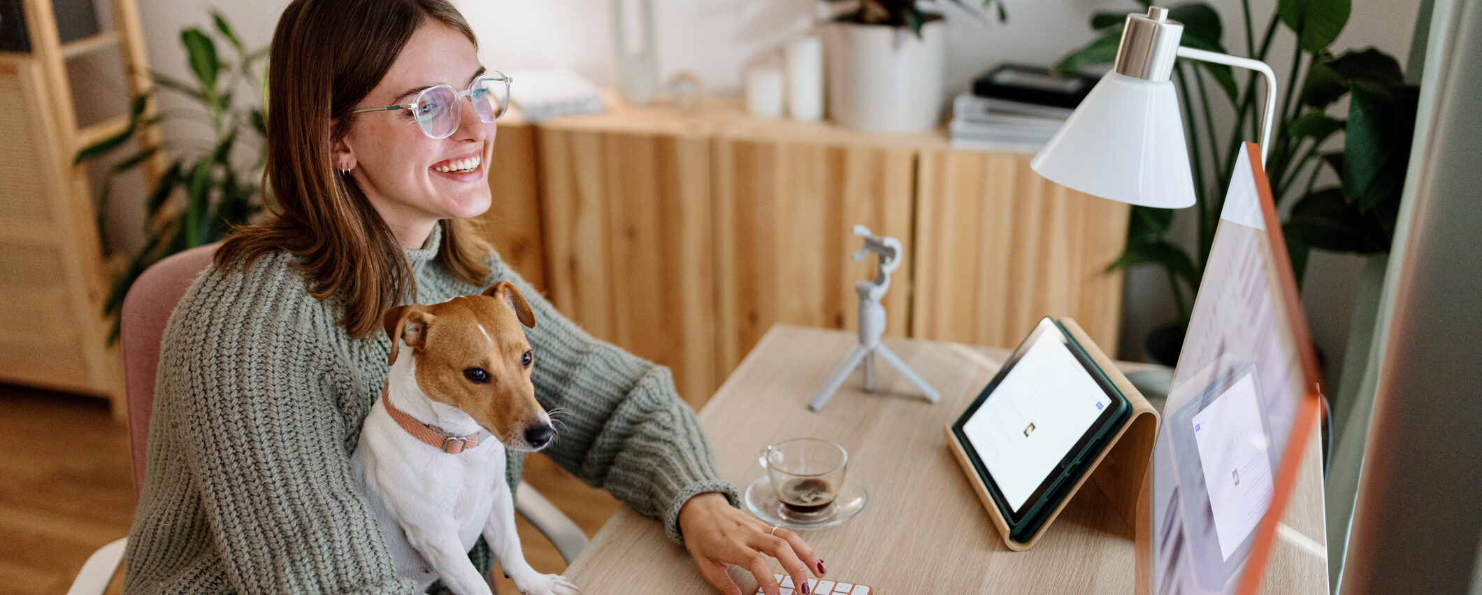 Woman with glasses sitting at a desk with a dog, both looking focused and engaged with the computer screen.